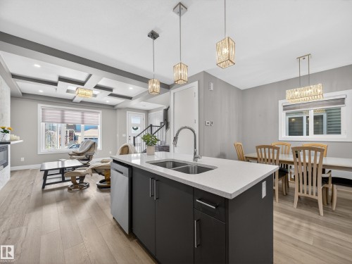 Kitchen with dark cabinetry, light wood finished floors, an island with sink, coffered ceiling, and dishwasher - 9358 Pear Link Link, Edmonton, AB - Indoor Photo Showing Kitchen With Double Sink With Upgraded Kitchen