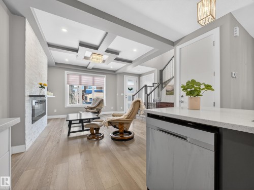 Interior space featuring a stone fireplace, coffered ceiling, light wood-style flooring, and recessed lighting - 9358 Pear Link Link, Edmonton, AB - Indoor Photo Showing Other Room