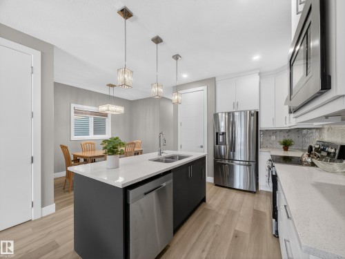 Dual tone kitchen with stainless steel appliances, two tone cabinets, an island with sink, light stone counters, and light wood-style floors - 9358 Pear Link Link, Edmonton, AB - Indoor Photo Showing Kitchen With Double Sink With Upgraded Kitchen
