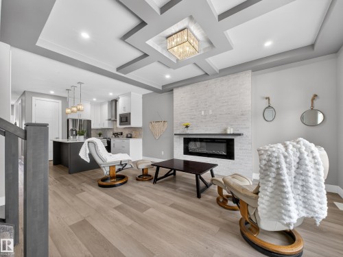 Living room featuring a chandelier, light wood-style flooring, coffered ceiling, and a fireplace - 9358 Pear Link Link, Edmonton, AB - Indoor Photo Showing Other Room With Fireplace