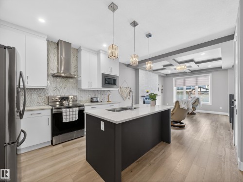 Two tone kitchen with stainless steel appliances, an island with sink, coffered ceiling, light wood-style floors, and hanging light fixtures - 9358 Pear Link Link, Edmonton, AB - Indoor Photo Showing Kitchen With Double Sink With Upgraded Kitchen