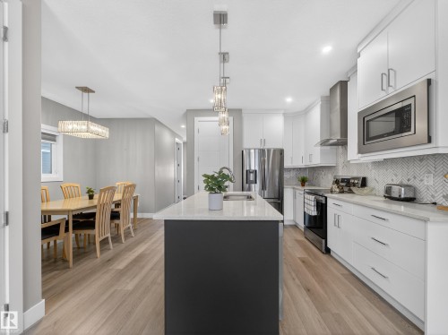 Two tone kitchen featuring stainless steel appliances, light stone countertops, a center island with sink, light wood-style floors, and two tone cabinets - 9358 Pear Link Link, Edmonton, AB - Indoor Photo Showing Kitchen With Upgraded Kitchen