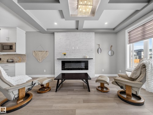 Living area with coffered ceiling, light wood finished floors, a stone fireplace, and suspended lighting - 9358 Pear Link Link, Edmonton, AB - Indoor Photo Showing Other Room With Fireplace