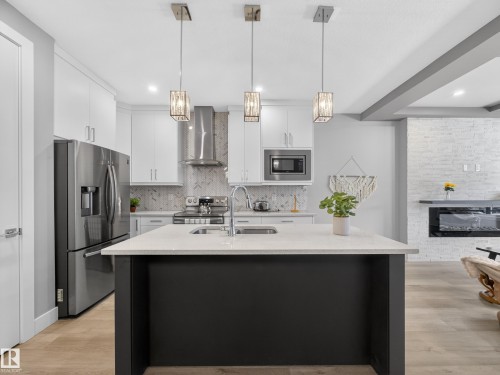 Kitchen featuring white cabinets, stainless steel appliances, a large fireplace, and pendant lighting - 9358 Pear Link Link, Edmonton, AB - Indoor Photo Showing Kitchen With Upgraded Kitchen