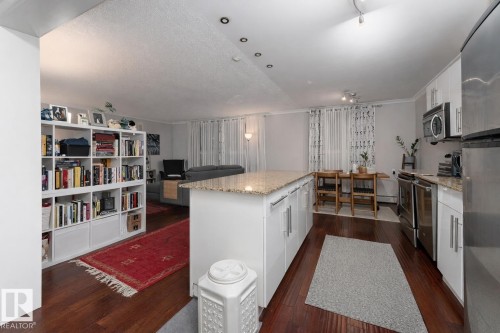 Kitchen featuring stainless steel appliances, white cabinets, dark wood-style flooring, light stone countertops, and crown molding - 7 10525 83 Avenue, Edmonton, AB - Indoor Photo Showing Kitchen