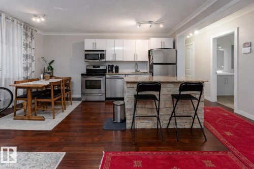 Kitchen with ornamental molding, stainless steel appliances, dark wood-type flooring, a center island, and a kitchen bar - 7 10525 83 Avenue, Edmonton, AB - Indoor Photo Showing Kitchen