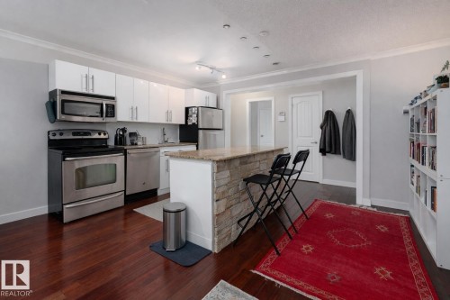 Kitchen featuring stainless steel appliances, a kitchen island, white cabinetry, dark wood-type flooring, and crown molding - 7 10525 83 Avenue, Edmonton, AB - Indoor Photo Showing Kitchen