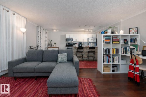 Living room with ornamental molding, dark wood-type flooring, and a textured ceiling - 7 10525 83 Avenue, Edmonton, AB - Indoor Photo Showing Living Room