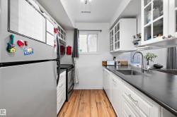 Kitchen with stainless steel appliances, white cabinetry, dark countertops, light wood-type flooring, and glass insert cabinets - 