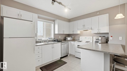 Kitchen featuring white appliances, white cabinetry, a peninsula, a breakfast bar, and track lighting - 401 636 Mcallister Loop, Edmonton, AB - Indoor Photo Showing Kitchen With Double Sink