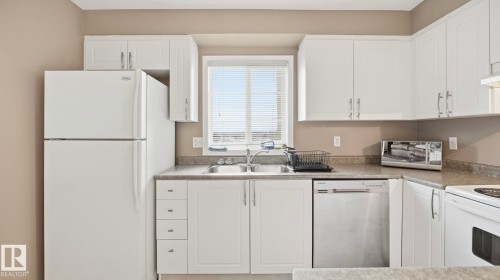 Kitchen with white appliances, white cabinetry, and light countertops - 401 636 Mcallister Loop, Edmonton, AB - Indoor Photo Showing Kitchen With Double Sink