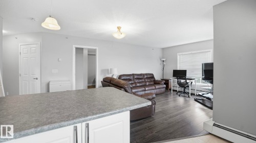 Living room with a baseboard radiator, an office area, and dark wood-style flooring - 401 636 Mcallister Loop, Edmonton, AB - Indoor