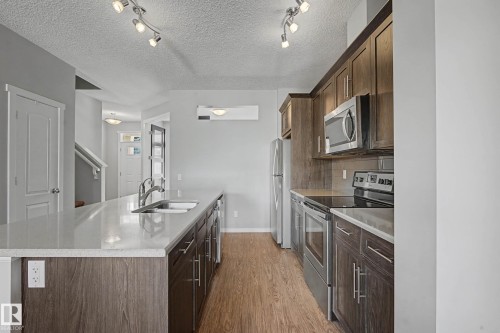 Kitchen featuring stainless steel appliances, a kitchen island with sink, dark wood finish cabinetry, backsplash, and track lighting - 2577 Coughlan Road, Edmonton, AB - Indoor Photo Showing Kitchen With Upgraded Kitchen