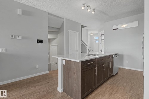 Kitchen with light countertops, light wood-style flooring, a kitchen island with sink, dark wood finish cabinets, and a textured ceiling - 2577 Coughlan Road, Edmonton, AB - Indoor Photo Showing Kitchen