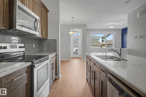 Kitchen featuring stainless steel appliances, light stone countertops, light wood-style floors, backsplash, and a textured ceiling - 2577 Coughlan Road, Edmonton, AB - Indoor Photo Showing Kitchen With Stainless Steel Kitchen With Double Sink With Upgraded Kitchen