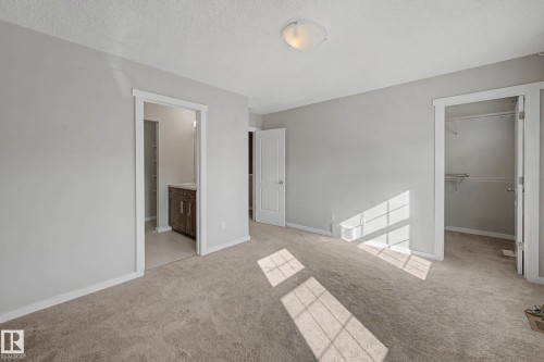 Unfurnished bedroom featuring a spacious closet, a textured ceiling, light carpet, and ensuite bathroom - 2577 Coughlan Road, Edmonton, AB - Indoor