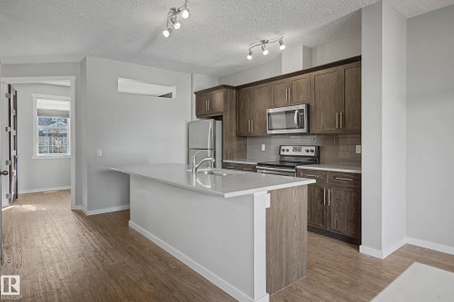 Kitchen featuring stainless steel appliances, a kitchen island with sink, decorative backsplash, light wood-style floors, and a textured ceiling - 2577 Coughlan Road, Edmonton, AB - Indoor Photo Showing Kitchen With Stainless Steel Kitchen With Upgraded Kitchen