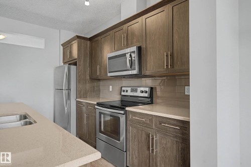 Kitchen featuring stainless steel appliances, decorative backsplash, dark wood finish cabinetry, a textured ceiling, and light stone countertops - 2577 Coughlan Road, Edmonton, AB - Indoor Photo Showing Kitchen With Stainless Steel Kitchen With Double Sink