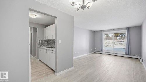 Kitchen featuring light countertops, white cabinets, decorative backsplash, light wood-style flooring, and a textured ceiling - 103 1624 48 Street, Edmonton, AB - Indoor Photo Showing Kitchen