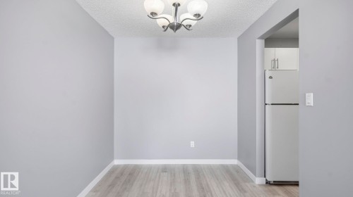 Unfurnished dining area featuring light wood-style flooring, a textured ceiling, and a chandelier - 103 1624 48 Street, Edmonton, AB - Indoor Photo Showing Other Room
