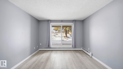 Spare room with a textured ceiling, light wood-type flooring, and a baseboard radiator - 103 1624 48 Street, Edmonton, AB - Indoor Photo Showing Other Room