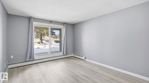 Spare room with a baseboard radiator, light wood-style flooring, and a textured ceiling - 103 1624 48 Street, Edmonton, AB - Indoor Photo Showing Other Room