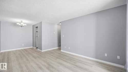 Unfurnished room featuring a chandelier, light wood-style flooring, and a textured ceiling - 103 1624 48 Street, Edmonton, AB - Indoor Photo Showing Other Room