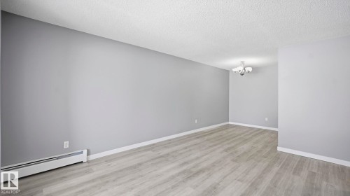 Empty room featuring baseboard heating, light wood-style flooring, a textured ceiling, and suspended lighting - 103 1624 48 Street, Edmonton, AB - Indoor Photo Showing Other Room