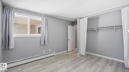 Unfurnished bedroom with baseboard heating, light wood finished floors, a textured ceiling, and a closet - 103 1624 48 Street, Edmonton, AB - Indoor