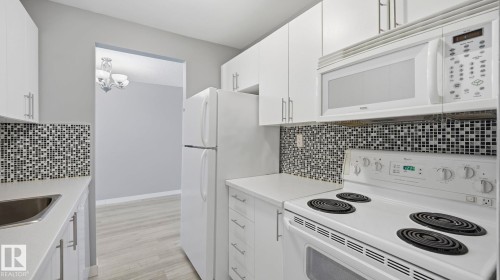 Kitchen featuring white appliances, white cabinetry, light countertops, and tasteful backsplash - 103 1624 48 Street, Edmonton, AB - Indoor Photo Showing Kitchen