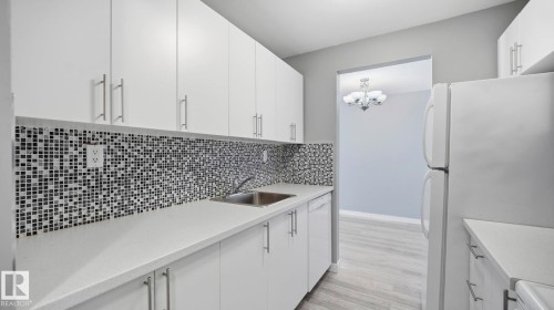 Kitchen with white cabinets, white appliances, decorative backsplash, light wood-style flooring, and hanging lights - 103 1624 48 Street, Edmonton, AB - Indoor Photo Showing Kitchen