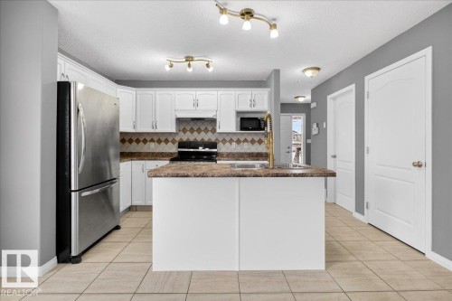 Kitchen with white cabinetry, freestanding refrigerator, electric stove, a textured ceiling, and tasteful backsplash - 150 Acacia Circle, Leduc, AB - Indoor Photo Showing Kitchen With Double Sink