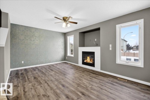 Unfurnished living room with a glass covered fireplace, wood finished floors, a textured ceiling, ceiling fan, and wallpapered walls - 150 Acacia Circle, Leduc, AB - Indoor Photo Showing Other Room With Fireplace