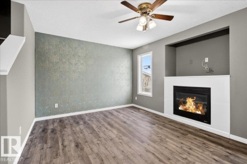 Unfurnished living room featuring wood finished floors, a textured ceiling, a glass covered fireplace, a ceiling fan, and an accent wall - 150 Acacia Circle, Leduc, AB - Indoor Photo Showing Living Room With Fireplace