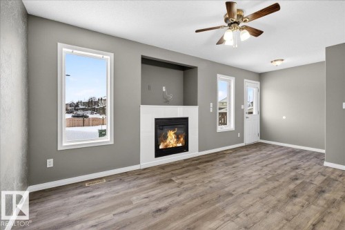 Unfurnished living room with wood finished floors, a tiled fireplace, and a ceiling fan - 150 Acacia Circle, Leduc, AB - Indoor Photo Showing Living Room With Fireplace