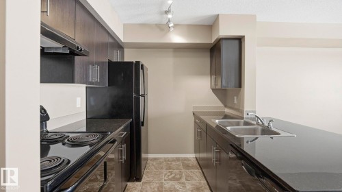 Kitchen with black appliances, dark wood finish cabinetry, a textured ceiling, dark stone countertops, and a peninsula - 319 274 Mcconachie Drive, Edmonton, AB - Indoor Photo Showing Kitchen With Double Sink