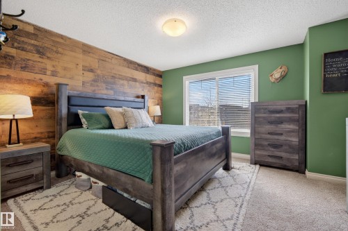 Bedroom with wooden walls, light carpet, a textured ceiling, and an accent wall - 7074 Cardinal Way, Edmonton, AB - Indoor Photo Showing Bedroom