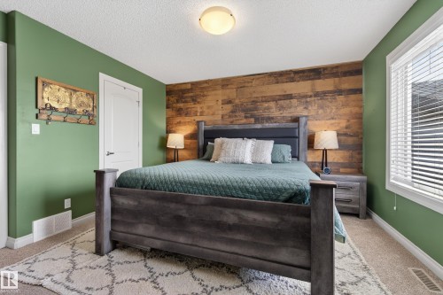 Carpeted bedroom featuring an accent wall, wood walls, and a textured ceiling - 7074 Cardinal Way, Edmonton, AB - Indoor Photo Showing Bedroom