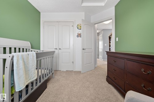 Bedroom with a textured ceiling, light carpet, a crib, and a closet - 7074 Cardinal Way, Edmonton, AB - Indoor Photo Showing Bedroom