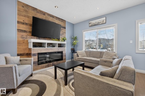 Living room with an accent wall, a glass covered fireplace, recessed lighting, wood finished floors, and a textured ceiling - 7074 Cardinal Way, Edmonton, AB - Indoor Photo Showing Living Room With Fireplace