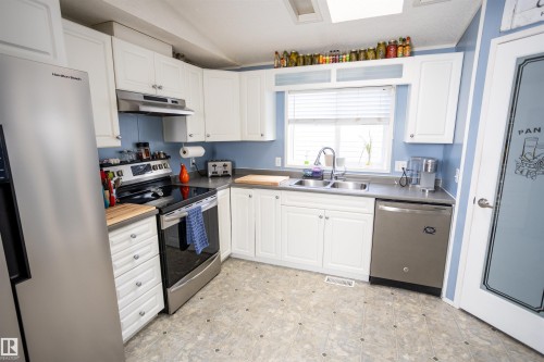 The kitchen features white cabinetry, a double basin sink, stainless steel appliances, and a window with blinds - 41 Graywood Cove, Stony Plain, AB - Indoor Photo Showing Kitchen With Double Sink
