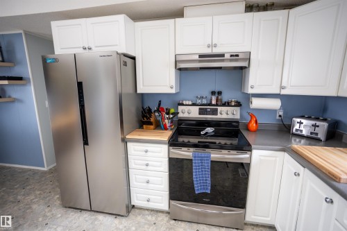 The kitchen features white cabinetry, a stainless steel side-by-side refrigerator, a stainless steel range with an overhead microwave, and gray countertops - 41 Graywood Cove, Stony Plain, AB - Indoor Photo Showing Kitchen
