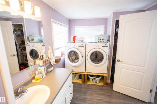 The property features a laundry room with two front-loading machines, a vanity with a sink and mirror, and wood-look flooring - 41 Graywood Cove, Stony Plain, AB - Indoor Photo Showing Laundry Room