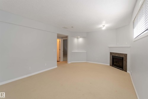 Unfurnished living room featuring light colored carpet, a tile fireplace, and a textured ceiling - 20604 48 Avenue, Edmonton, AB - Indoor Photo Showing Other Room With Fireplace