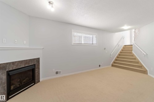 Basement featuring carpet, a tiled fireplace, and a textured ceiling - 20604 48 Avenue, Edmonton, AB - Indoor With Fireplace