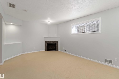 Unfurnished living room featuring light colored carpet, a fireplace, and a textured ceiling - 20604 48 Avenue, Edmonton, AB - Indoor With Fireplace