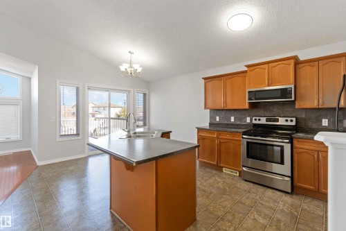 Kitchen with stainless steel appliances, dark countertops, a kitchen island with sink, and hanging lights - 20604 48 Avenue, Edmonton, AB - Indoor Photo Showing Kitchen With Double Sink