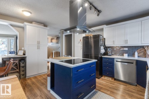 Kitchen with dual tone cabinets, island exhaust hood, a textured ceiling, stainless steel appliances, and light wood-type flooring - 14 Lester Crescent, St. Albert, AB - Indoor Photo Showing Kitchen