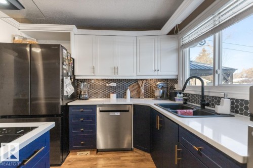 Dual tone kitchen featuring dual tone cabinetry, stainless steel appliances, light wood-style floors, a textured ceiling, and ornamental molding - 14 Lester Crescent, St. Albert, AB - Indoor Photo Showing Kitchen With Double Sink