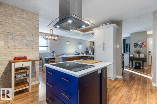 Dual tone kitchen featuring island exhaust hood, a kitchen island, light wood finished floors, black electric stovetop, and a textured ceiling - 14 Lester Crescent, St. Albert, AB - Indoor Photo Showing Kitchen